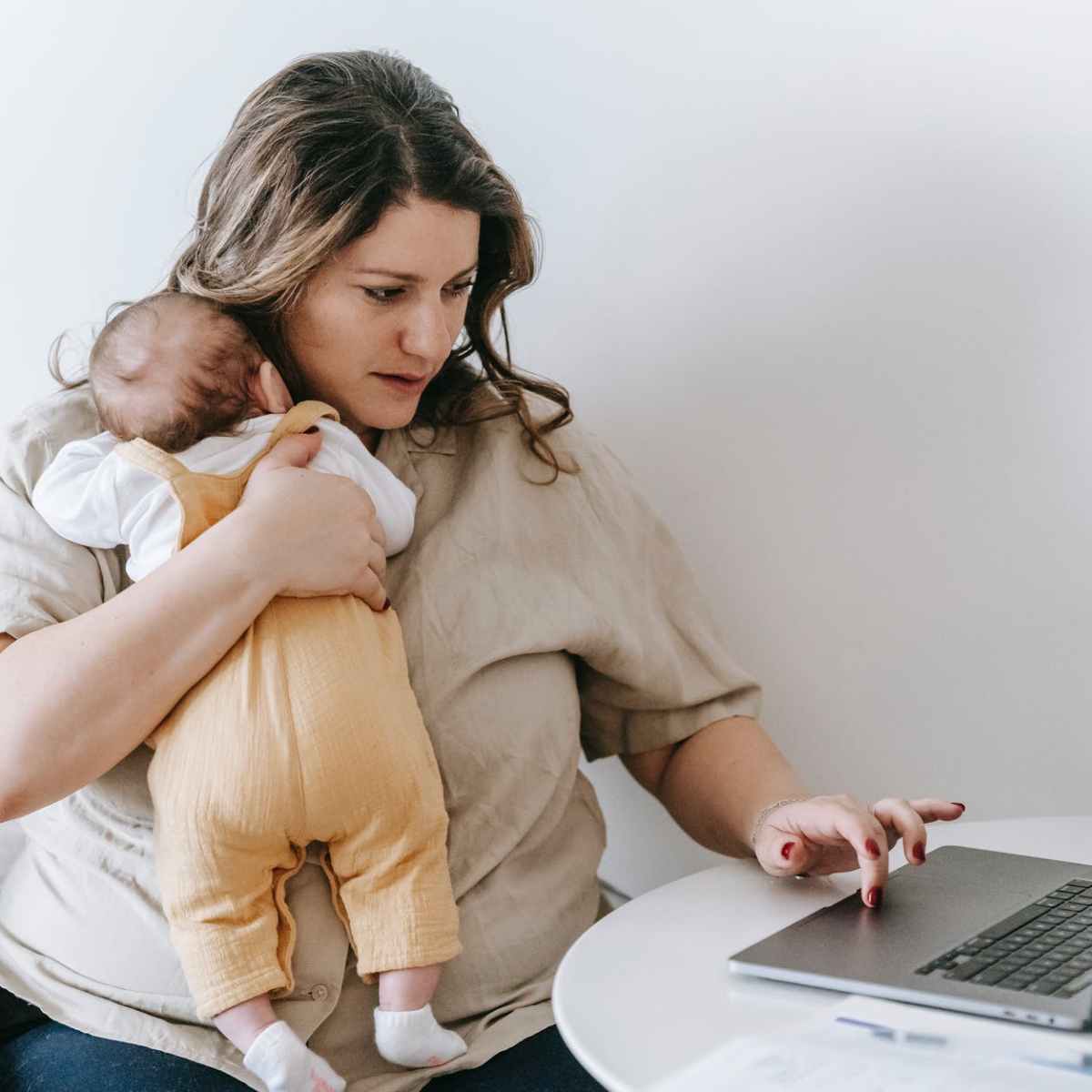 young working mother cuddling infant and using laptop at home